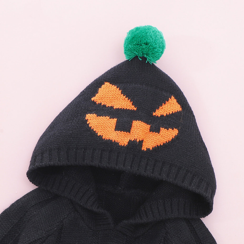 Black knit baby outfit with Halloween pumpkin face design on a pink background.