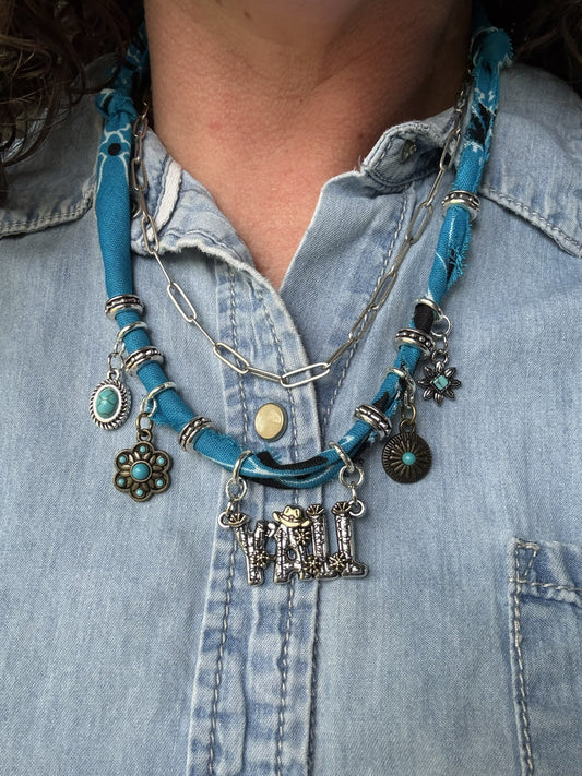 Close-up of a person wearing a blue fabric necklace with various charms on a denim shirt.