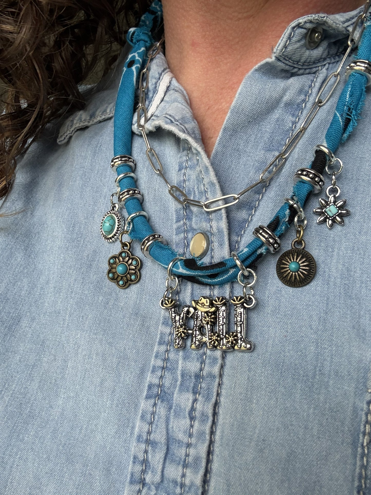 Necklace with blue cord and various charms worn over a denim shirt