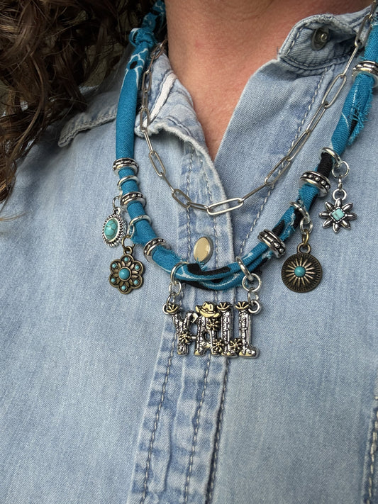 Necklace with blue cord and various charms worn over a denim shirt