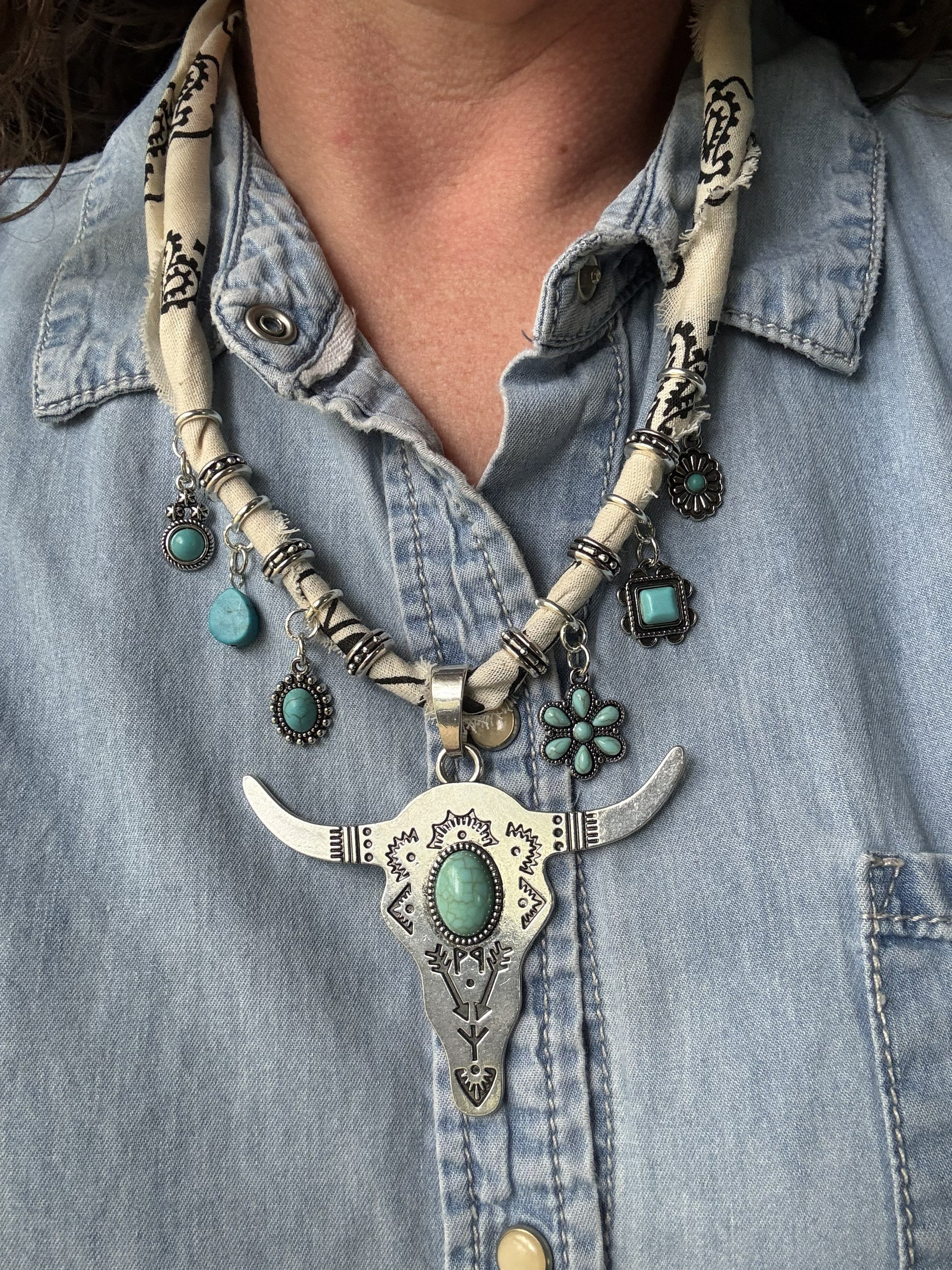 Necklace with bull head pendant and turquoise stones worn by a person in a denim shirt.