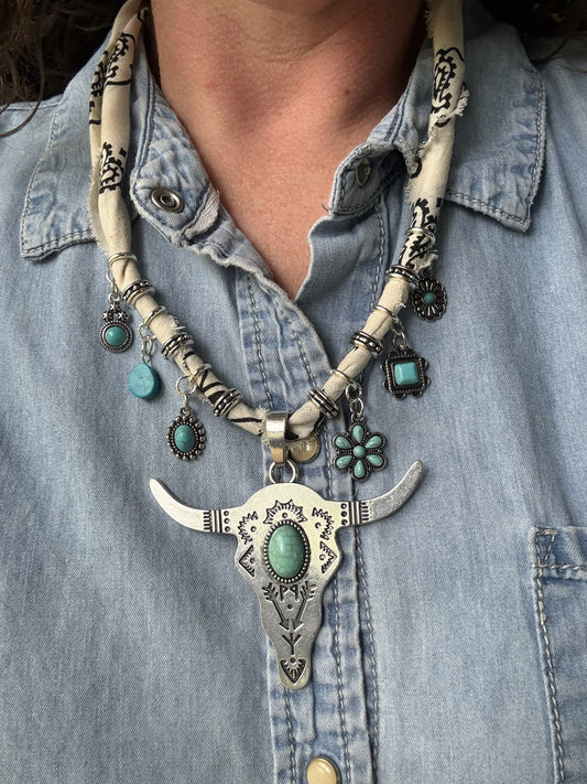 Necklace with bull head pendant and turquoise stones worn by a person in a denim shirt.
