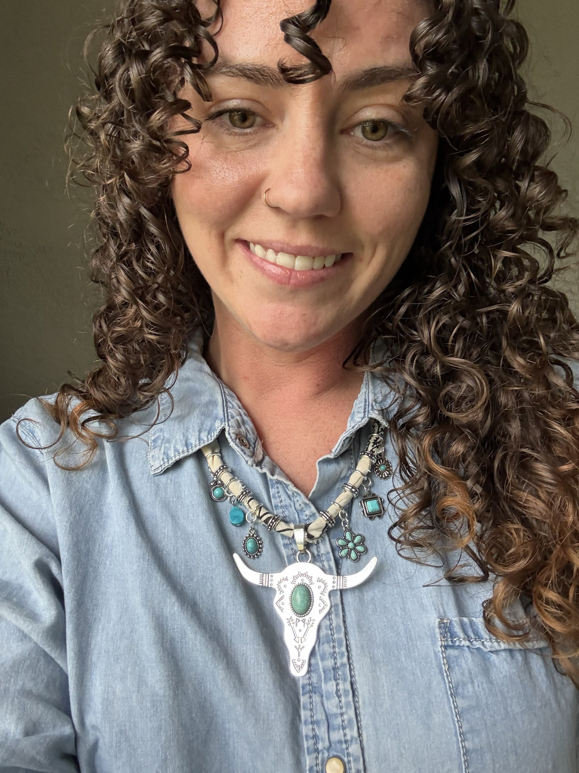 Woman with curly hair wearing a blue denim shirt and a decorative necklace.