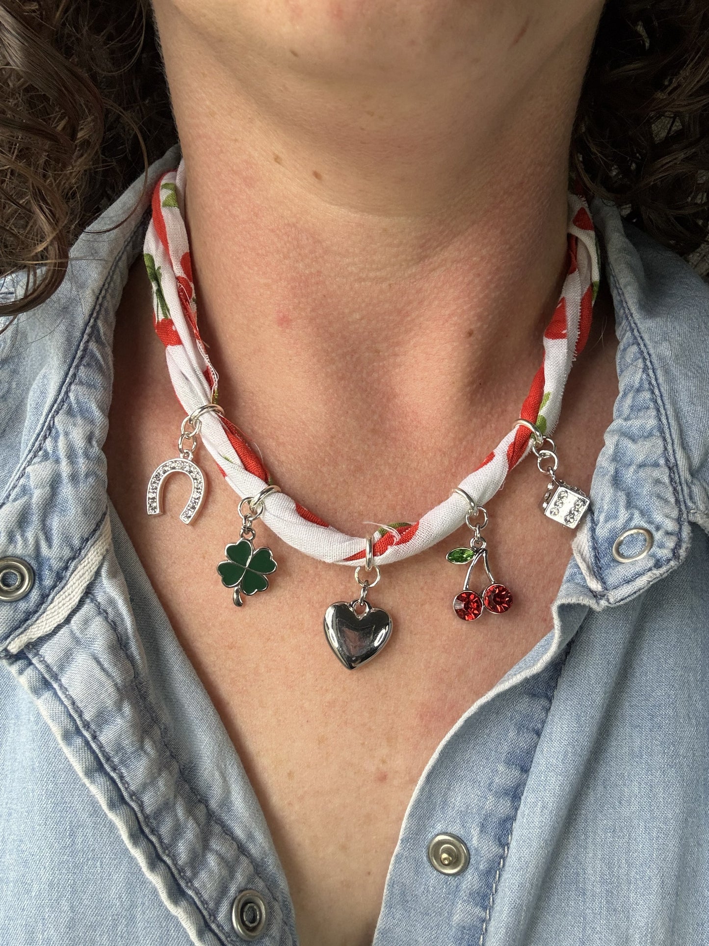 Necklace with various charms worn by a person in a denim jacket.