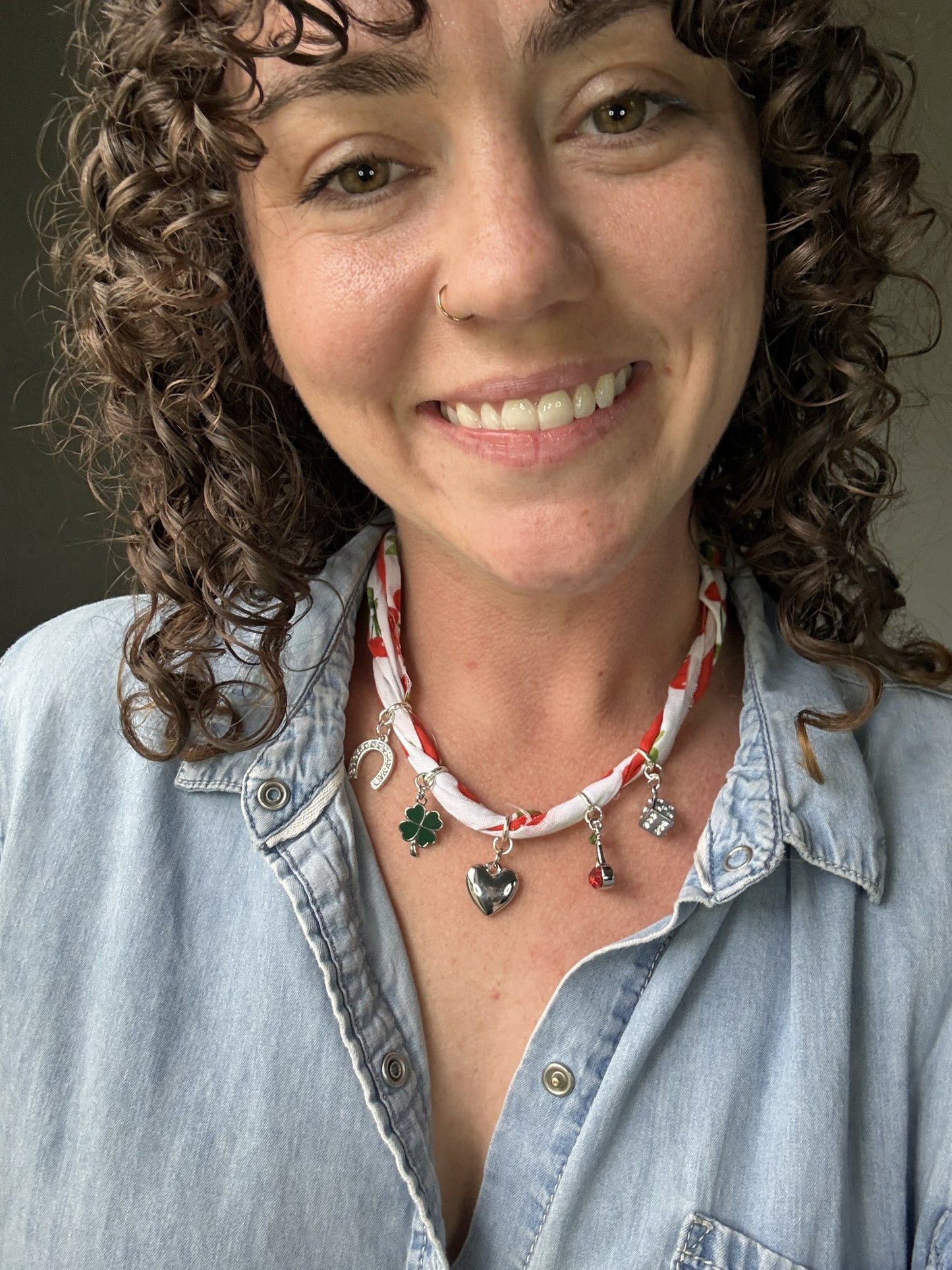 Woman wearing a denim shirt and a necklace with various pendants against a neutral background