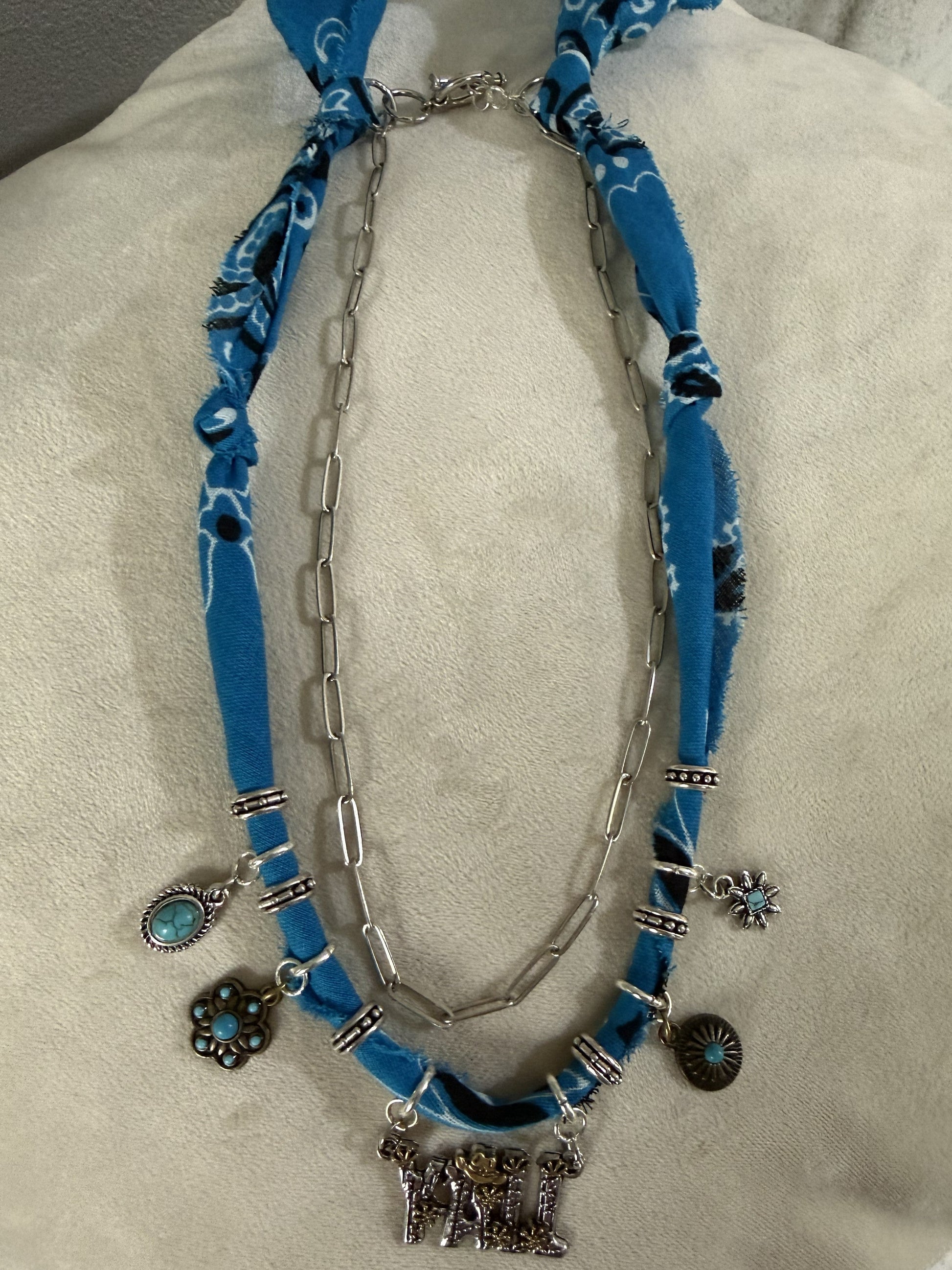 Necklace with blue fabric and silver charms on a mannequin bust.