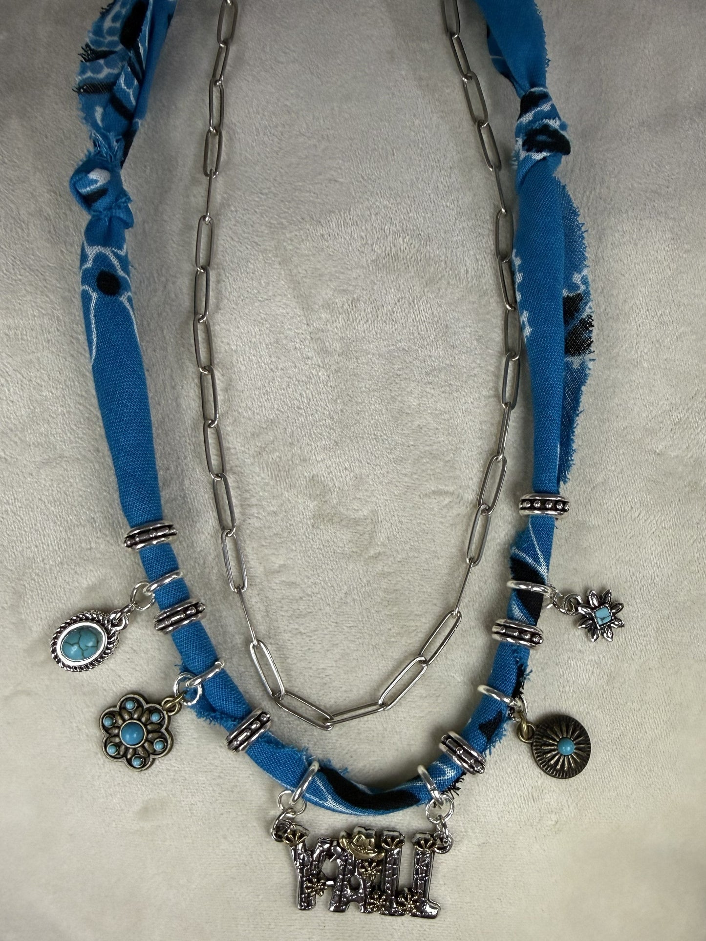 Blue fabric necklace with silver chain and charms on a white surface