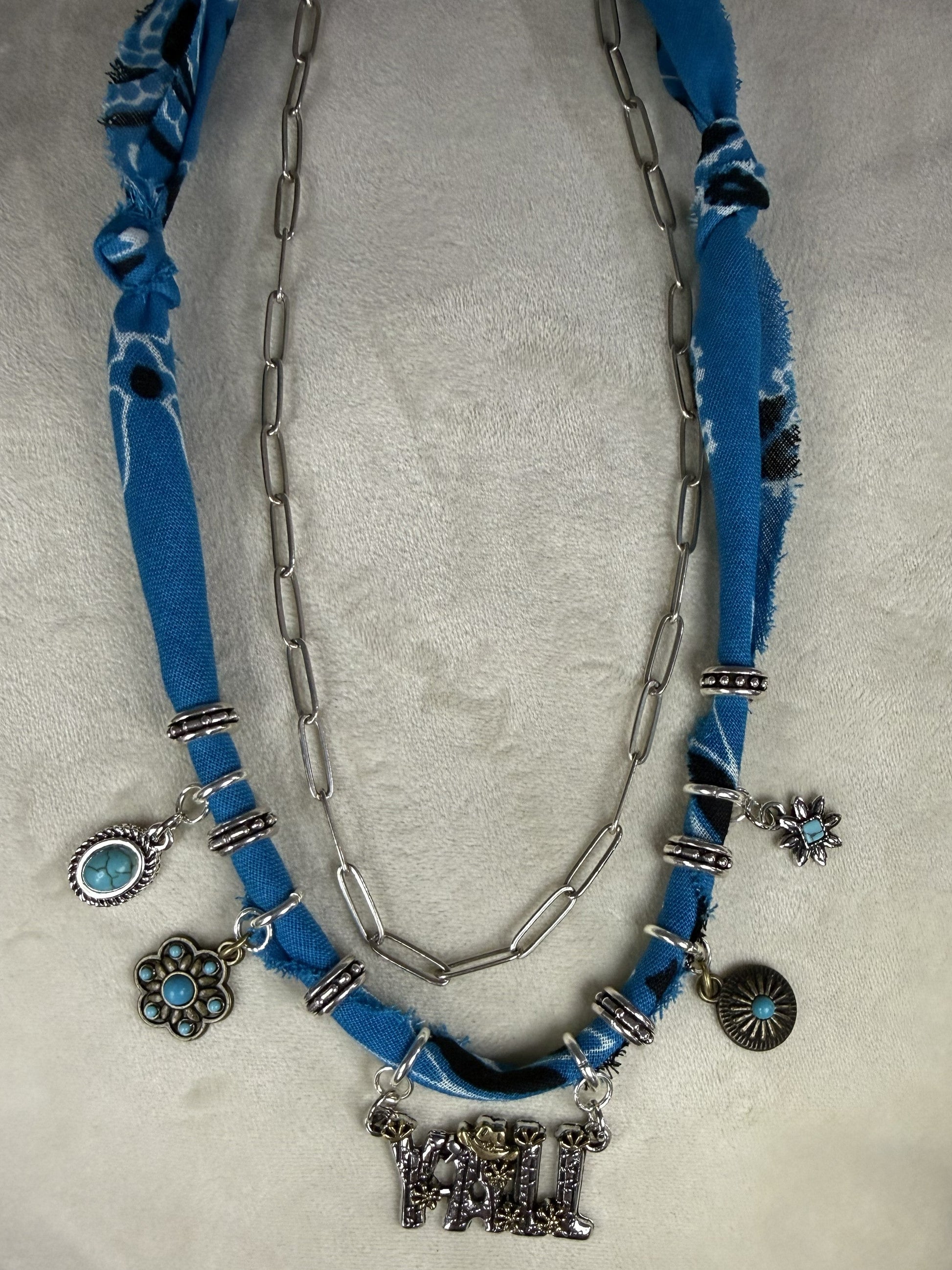 Blue fabric necklace with silver chain and charms on a white surface