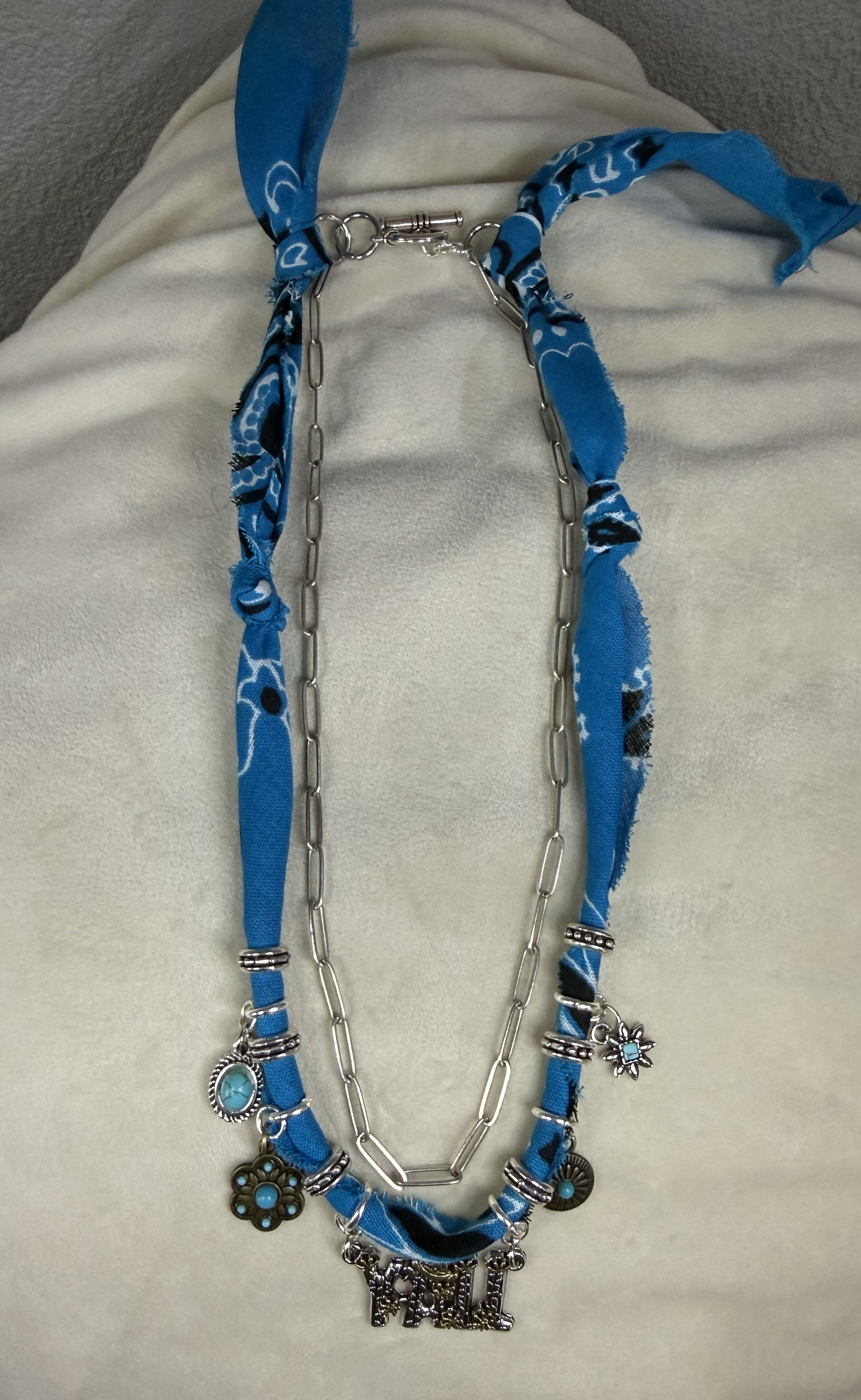 Necklace with blue fabric strap and silver chain on a white surface