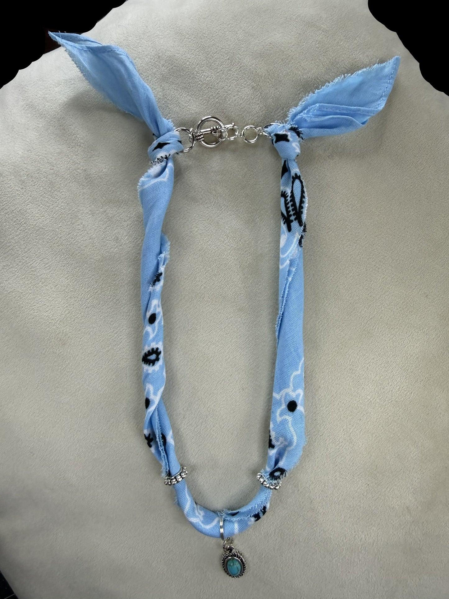 Necklace with blue fabric wrap and pendant on a mannequin bust.