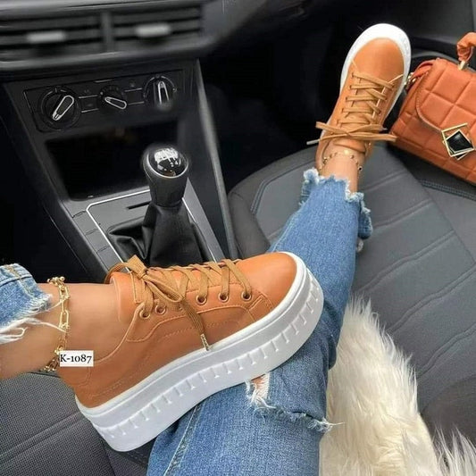 Brown sneakers with white soles worn inside a car, paired with ripped jeans.