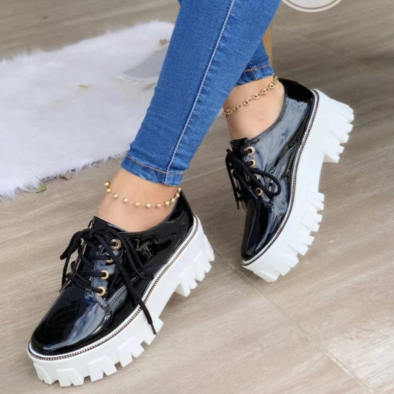 A pair of black Elevation Oxford Platforms with a thick platform sole and a classic oxford lace-up design worn by a person with denim pants.