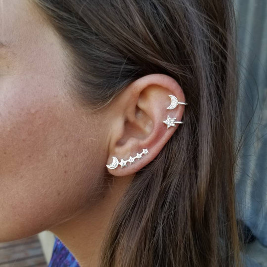 Close-up of an ear with multiple silver earrings against a neutral background