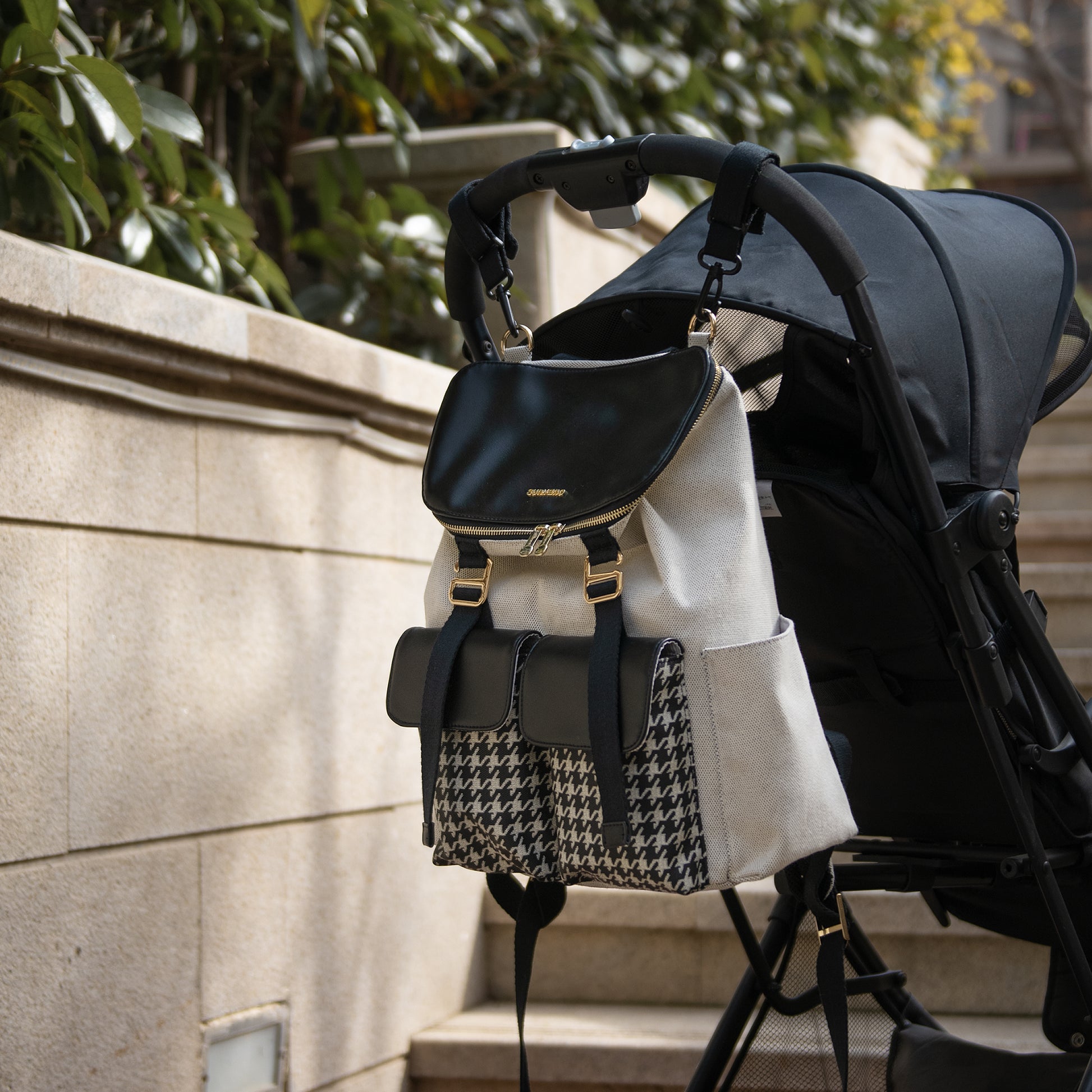 Black backpack with gold accents attached to a stroller against a stone wall background