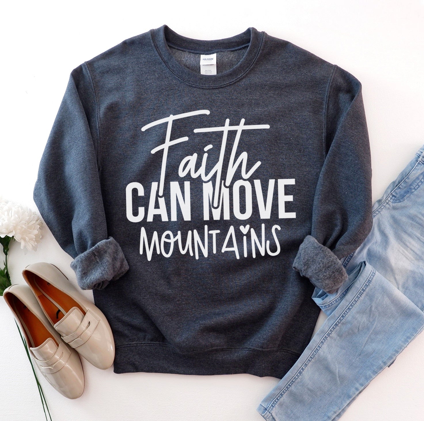 Dark blue sweatshirt with 'Faith Can Move Mountains' text, paired with jeans and shoes on a light background