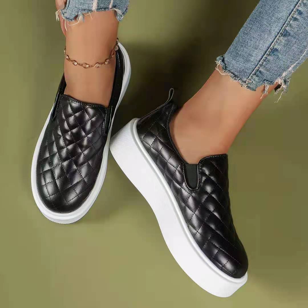 A pair of black slip-on casual platform shoes with a quilted pattern and thick platform sole, worn by a person with jeans.