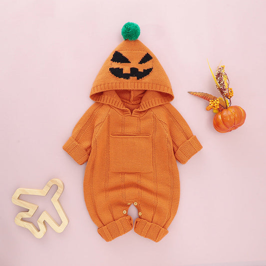 An orange baby romper with a monster print, including a hood with a spooky face design, displayed next to a small decorative pumpkin and a Halloween-themed pin.
