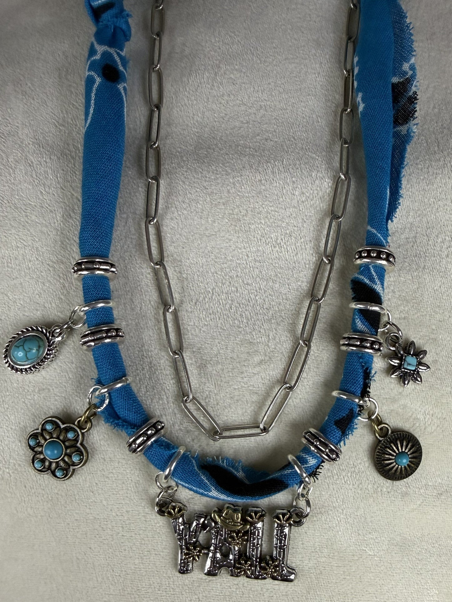 Necklace with blue fabric and silver charms on a gray background