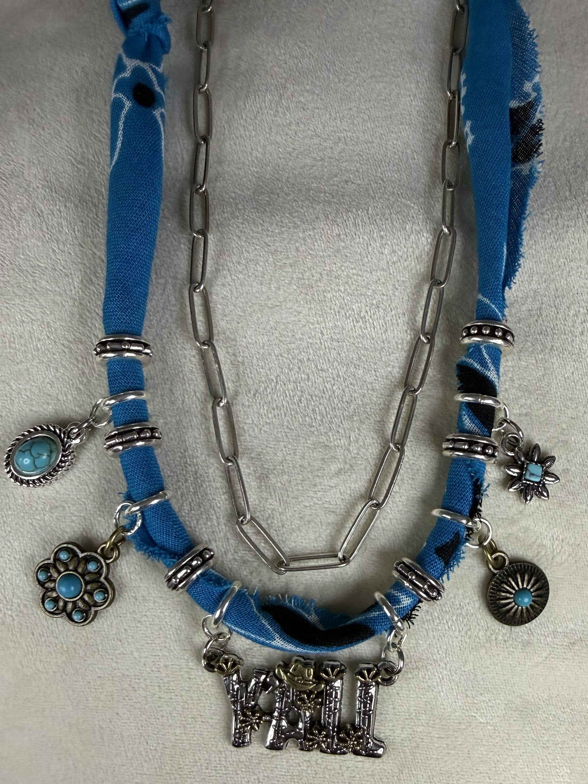 Necklace with blue fabric and silver charms on a gray background